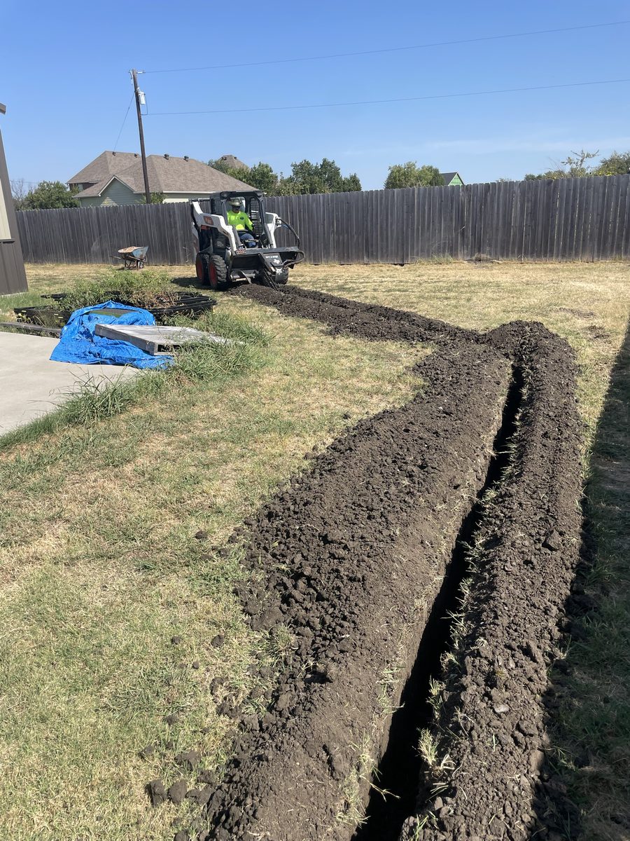 Skid steer cutting a curved drainage trench across a yard